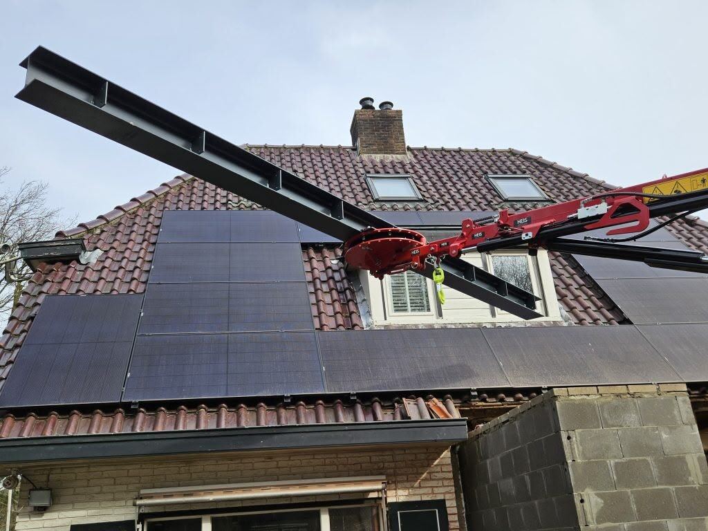 Balkendrukker aan de mini hijskraan schuift een stalen ligger door een dakraam